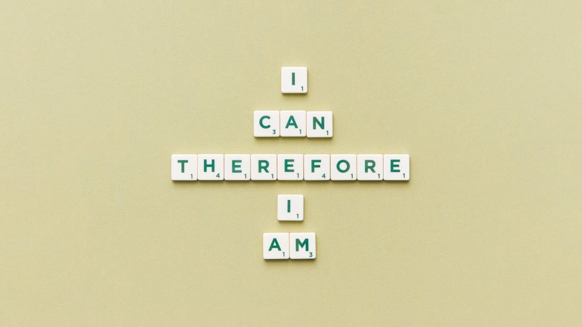 Inspirational phrase 'I Can Therefore I Am' arranged using Scrabble tiles on a green background.